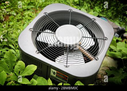 Modern Air conditioner in grown greenery on background,  top view with warning sign for safety. Stock Photo