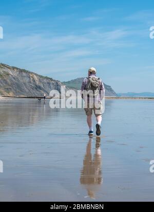 Charmouth Dorset, UK. 8th May, 2020. UK Weather: A hot and sunny bank holiday afternoon at Charmouth, West Dorset. Despite the beautiful weather he beaches remain quiet on the 75th aniversary of VE day as people continue to follow advice to stay at home during the coronavirus pandemic lockdown. A man walks on the deserted beach. Credit: Celia McMahon/Alamy Live News Stock Photo