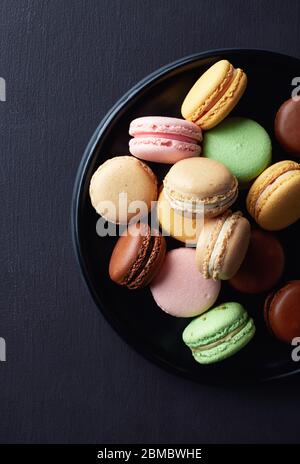 Black plate of colorful macarons on dark background. Top view Stock Photo