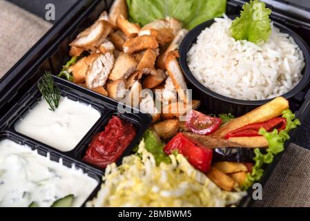 Traditional doner kebab in a black plastic container, sour cream, white boiled rice, roast meat, chiken, sauces, salad, cabbage and roasted vegetables Stock Photo