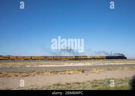 A steam engine belches smoke pulling a passenger train through desert Stock Photo