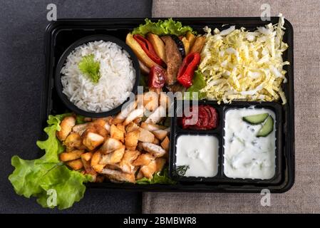 Traditional doner kebab in a black plastic container, sour cream, white boiled rice, roast meat, chiken, sauces, salad, cabbage and roasted vegetables Stock Photo