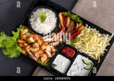 Traditional doner kebab in a black plastic container, sour cream, white boiled rice, roast meat, chiken, sauces, salad, cabbage and roasted vegetables Stock Photo