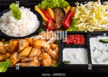 Traditional doner kebab in a black plastic container, sour cream, white boiled rice, roast meat, chiken, sauces, salad, cabbage and roasted vegetables Stock Photo