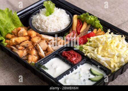 Traditional doner kebab in a black plastic container, sour cream, white boiled rice, roast meat, chiken, sauces, salad, cabbage and roasted vegetables Stock Photo