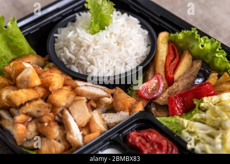 Traditional doner kebab in a black plastic container, sour cream, white boiled rice, roast meat, chiken, sauces, salad, cabbage and roasted vegetables Stock Photo