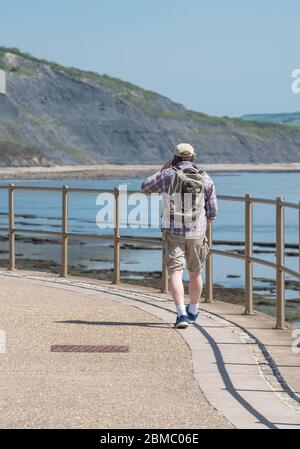 Lyme Regis Dorset, UK. 8th May, 2020. UK Weather: A hot and sunny bank holiday afternoon at Lyme Regis, West Dorset. A man walks along the seafront towards Charmouth. Credit: Celia McMahon/Alamy Live News Stock Photo