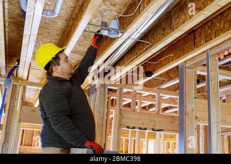 Electrician worker in installing a spotlight in the room on wooden beamed ceiling Stock Photo