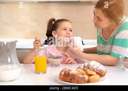 Mother having breakfast with her daughter at a table in kitchen, happy single mother concept Stock Photo