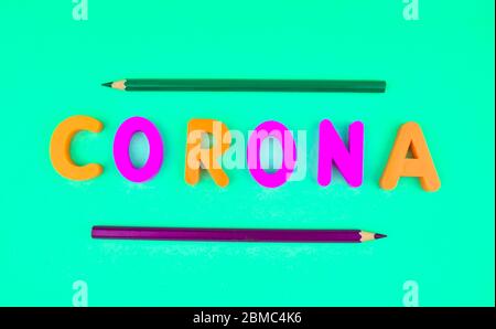 Corona word written with different colored letter blocks in the middle of two pencil crayons Stock Photo