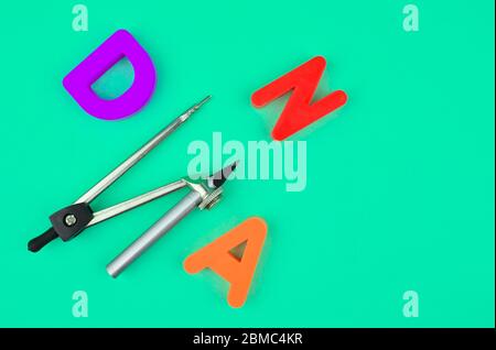 D N and A letters and a silver compass attached to a pencil placed on a blue paper background Stock Photo