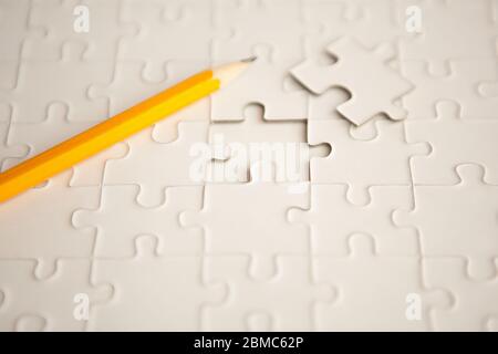 yellow pencil, puzzle with missing piece - solution concept. plan white puzzle surface texture with copy space. Stock Photo