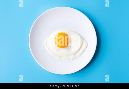 Breakfast, fried egg, yolk, omelet on white plate with color table, creative picture Stock Photo
