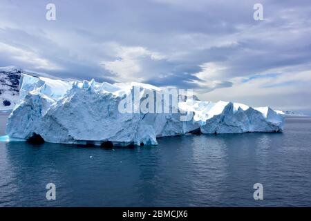 A large strange shaped iceberg floating in the cold waters of Antarctica, with a dramatic sky. Stock Photo