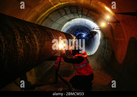 Worker in protective mask welding pipe in tunnel Stock Photo