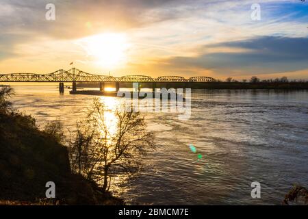 Sunset landscape of the Mississippi River bridge between Mississippi and Louisiana, in Vicksburg, MS, with towboat pushing barges. Stock Photo