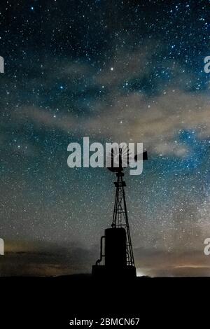 Windmill against vast starry sky, including the Milky Way and wispy clouds, above City of Rocks State Park, located between Silver City and Deming in Stock Photo