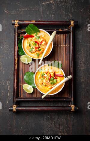 Shrimps Tom Yam Kung in white bowls on autentic thai tray top view, wooden background Stock Photo
