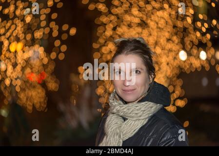 Portrait of a happy young woman in front of Christmas lights Stock Photo