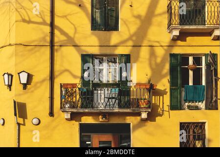Empty sunlit balcony on traditional yellow Italian house with shadow of tree, Verona, Italy Stock Photo