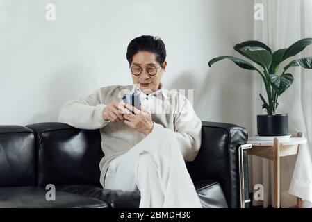 An Asian elderly man using mobile phone in the living room Stock Photo