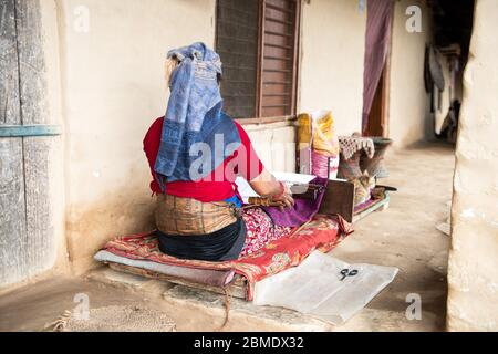 One woman weaving on a simple loom, sitting on a porch in a mountain village in Nepal. Stock Photo