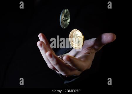 Male hand throwing two bitcoins up in the air on black background - closeup Stock Photo