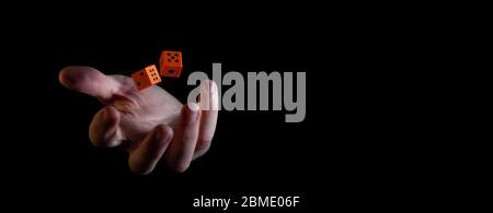 Two orange dice cubes thrown in the air above caucasian male hand against black background - narrow banner with copy space Stock Photo