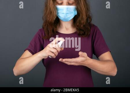 young girl in a blue medical mask holds a bottle with antibacterial spray,  disinfects hands with antiseptic. hygiene, coronavirus infection preventio Stock Photo