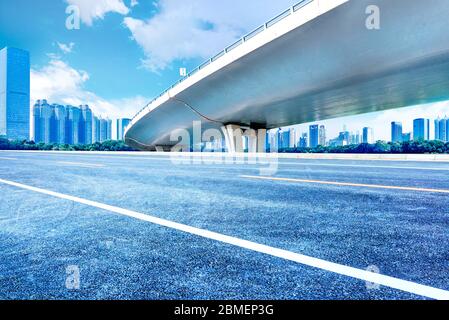 Under the overpass, car-free asphalt road, modern city building skyline as background. Stock Photo
