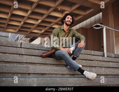 Handsome young man eating sandwich while sitting on stairs during break while looking away Stock Photo