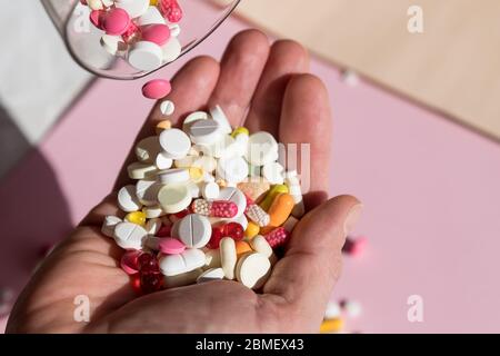 man Pouring capsules from a pill bottle ,holding pills on hand.Overdose of medication. A lot of pills spilled on table. Attempt of suicide.Economic Stock Photo