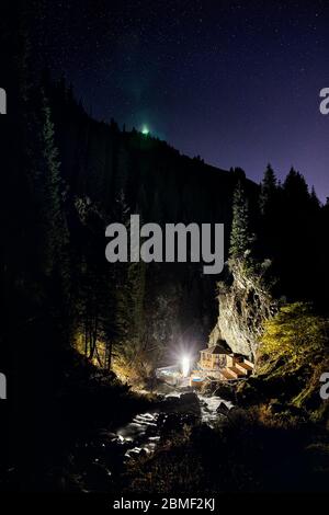 Big led Lamp glowing at wooden platform for camping near river in the mountains under night sky with stars Stock Photo