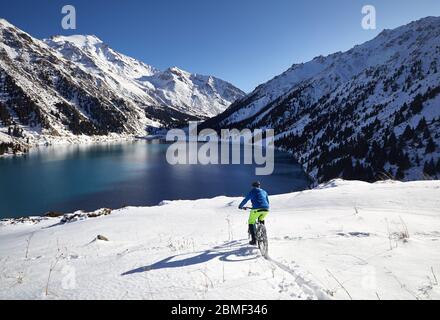 Cyclist rides at snow Shore of Mountain Lake in Almaty, Kazakhstan