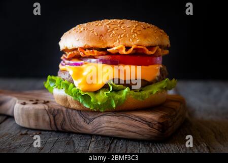 Hamburger with cheese, bacon, tomato and lettuce on dark wooden background Stock Photo