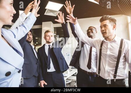 Close up top view of young people putting their hands together. A team of young businessmen working and communicating together in an office. Corporate Stock Photo