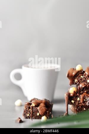 Stack of a brownie pieces with hazelnut, palm and cup on a grey table with gray background. Stock Photo