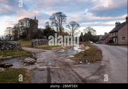 A stream runs past traditional cottages and the parish church of Crosby Ravensworth in Cumbria's Eden Valley. Stock Photo