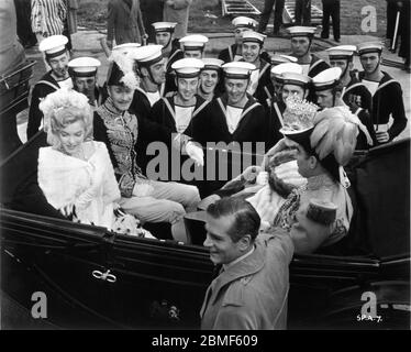 MARILYN MONROE RICHARD WATTIS SYBIL THORNDIKE and Director LAURENCE OLIVIER with Group of Sailors on set candid during filming of THE PRINCE AND THE SHOWGIRL 1957 director LAURENCE OLIVIER play and screenplay TERENCE RATTIGAN UK-USA co-production Marilyn Monroe Productions / Warner Bros. Stock Photo