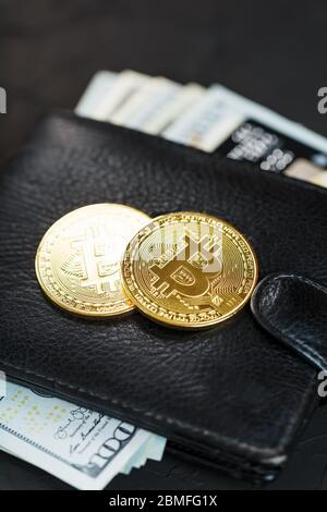 A black wallet with dollars, e-cards and bitcoins on a black textured background. Symbol of prosperity and prosperity. Close up Stock Photo