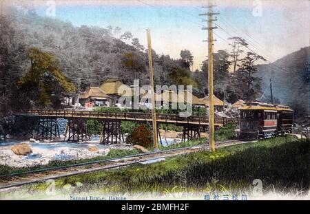 [ 1900s Japan - Train in Japanese Countryside ] —   A train rides along the Hayakawa River (早川) at Sanmaibashi (三枚橋) in Hakone, Kanagawa Prefecture. At the back, teahouses with thatched roofs are visible.  20th century vintage postcard. Stock Photo