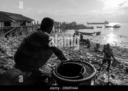 Low tide and people are searching for edibles or re-usable materials, amongst the waste that has landed on the beach. Sittwe, Myanmar Stock Photo