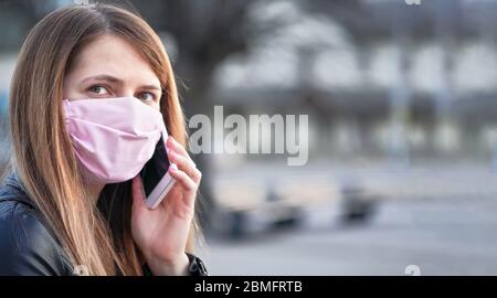 Young woman with pink cotton hand made face nose mouth mask talking over her mobile phone, close portrait, space on right side. Can be used during cor Stock Photo
