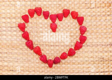 Ripe raspberries lying in the shape of a heart on a wicker mat Stock Photo