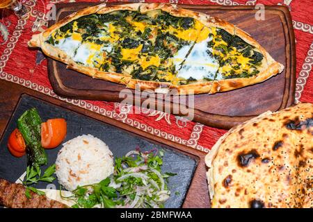 Traditional autyhentic turkish lunch or dinner: kebab with rice and vegetables, spinach and egg pide, pita flat bread and puff hot lavash or lavas hom Stock Photo