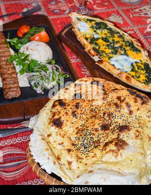 Traditional autyhentic turkish lunch or dinner: kebab with rice and vegetables, spinach and egg pide, pita flat bread and puff hot lavash or lavas hom Stock Photo