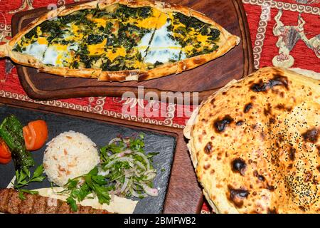 Traditional autyhentic turkish lunch or dinner: kebab with rice and vegetables, spinach and egg pide, pita flat bread and puff hot lavash or lavas hom Stock Photo