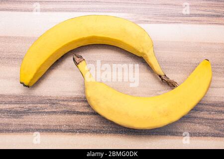 Two yellow bananas sitting symmetrical on a wooden table seen from above Stock Photo