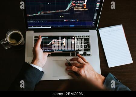 stock market trader analyzing bitcoin price trend. Investment broker trading bitcoin crypto currency using phone and laptop. Multiple devices. Stock Photo