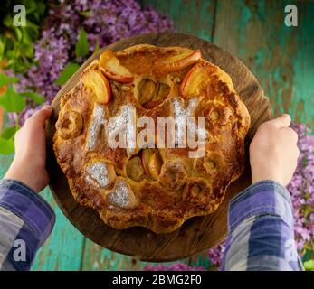 Hold a round homemade pie in your hands. Put on the table. A bouquet of lilacs. The letters MK . Simple pastry made from shortcrust pastry and Stock Photo